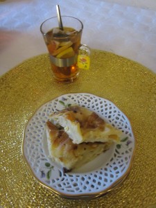 På bilden ser vi en assiett med två bitar ostkaka och ett te-glas med fruktbitar och te.