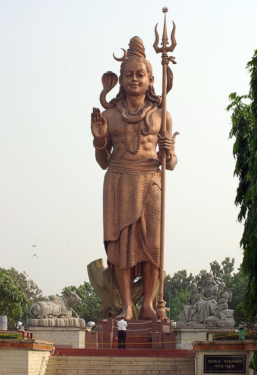 På ilden ser vi en stor skulptur av guden Shiva. I ena handen håller han en tre-udd. Skulpturen står i en park.